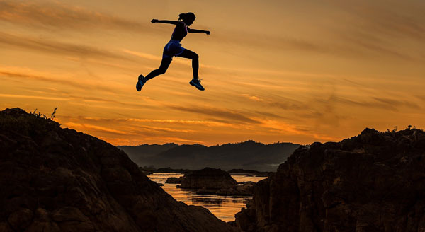 Person confidently jumping across rocks by the sea at sunset